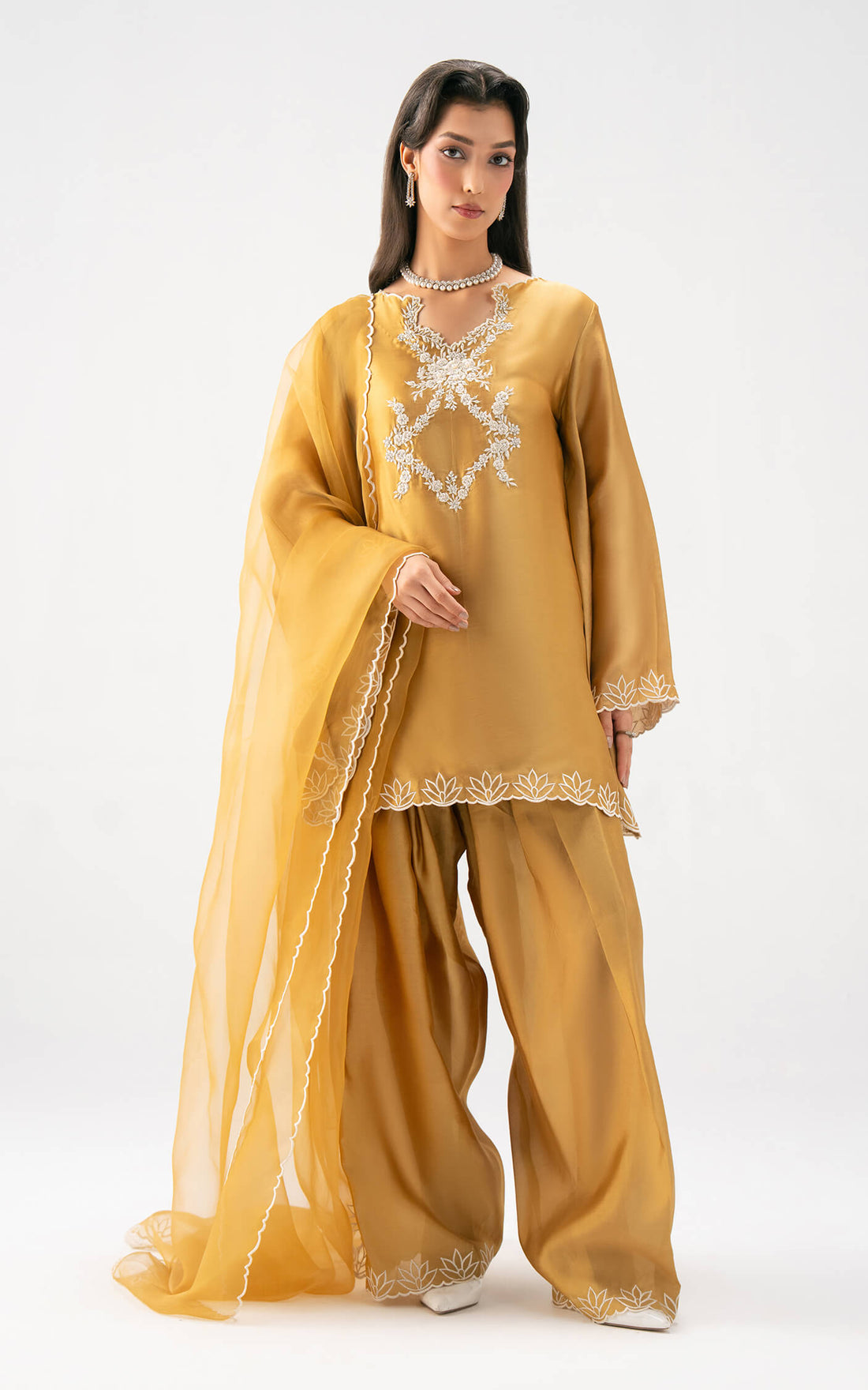 Woman wearing a mustard yellow traditional silk outfit with intricate white embroidery on a white background