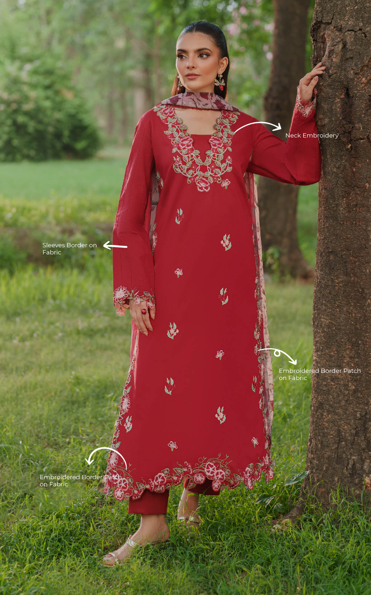 Woman in a red embroidered outfit standing in a grassy area with trees.
